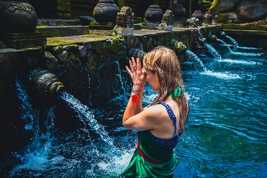 A visitor performing the purification ritual at Tirta Empul Temple, standing in front of the sacred water spouts and offering a prayer as part of the cleansing ceremony.