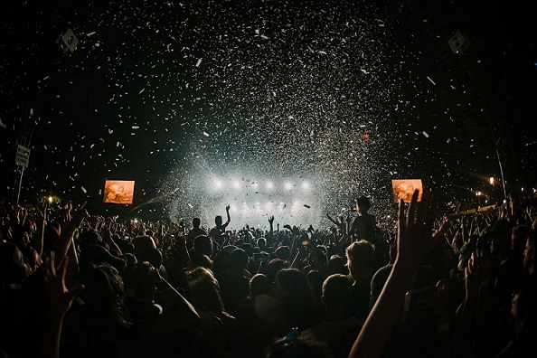 A large crowd enjoying a vibrant music festival, with confetti filling the air under bright stage lights, creating an energetic atmosphere.