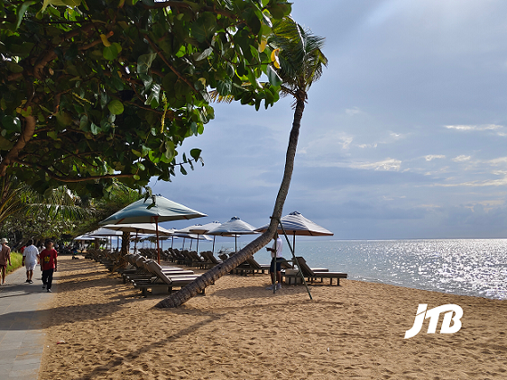 A tranquil view of Sanur Beach in Bali, showcasing soft golden sand, shaded loungers under umbrellas, and a calm ocean horizon